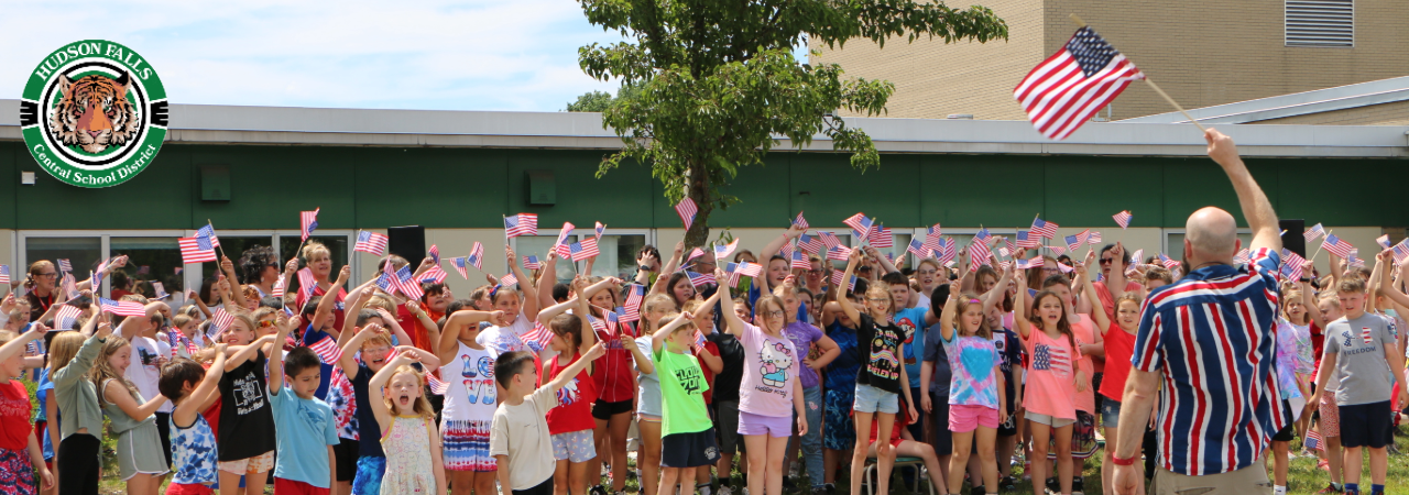Photo of the Primary School outside in a large group waving American Flags for Flag day celebration